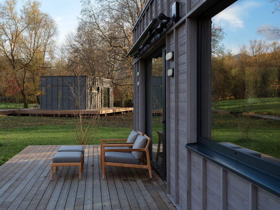 Holzdeck mit Liegestühlen einer Dwellii-Kabine, zweite Kabine jenseits der Wiese im goldenen Abendlicht