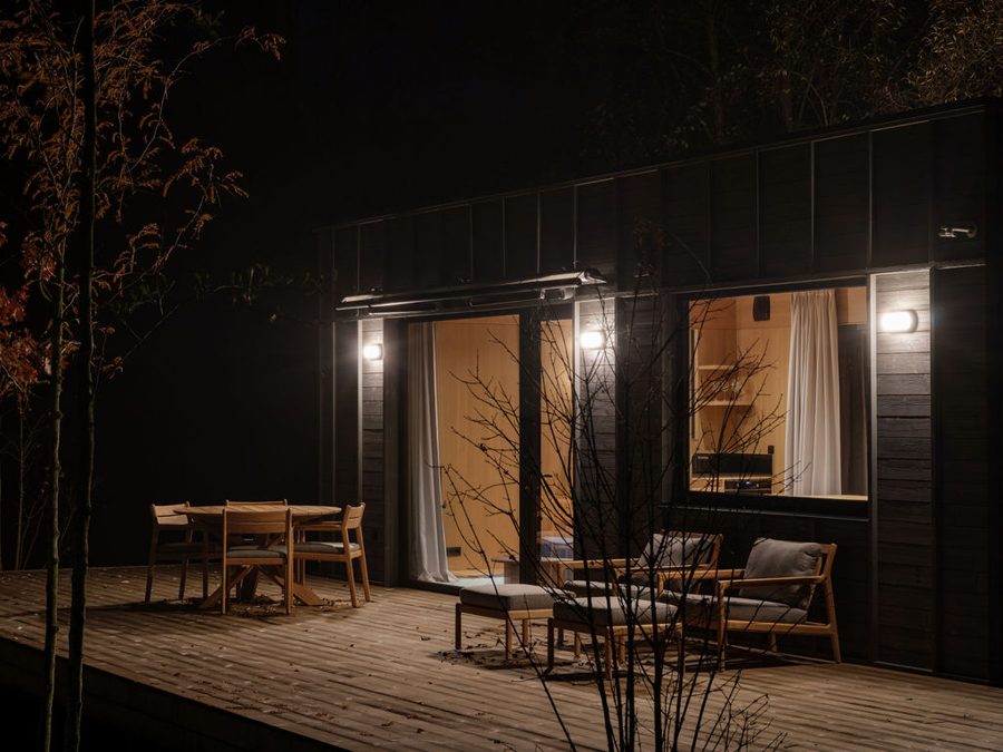 Dwellii-Kabine bei Nacht: warm erleuchteter Innenraum und beleuchtete Terrasse mit Essgruppe