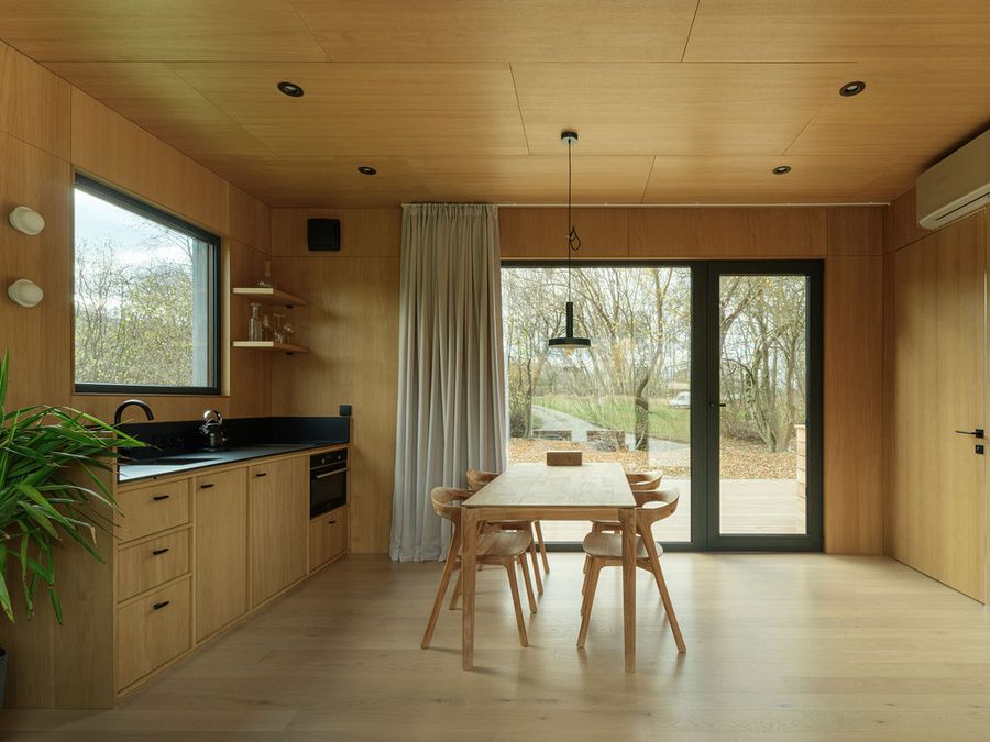 Holzverkleidete Küche einer Dwellii-Kabine: Eichenfronten, schwarze Arbeitsplatte, Esstisch, Glastür zum Deck