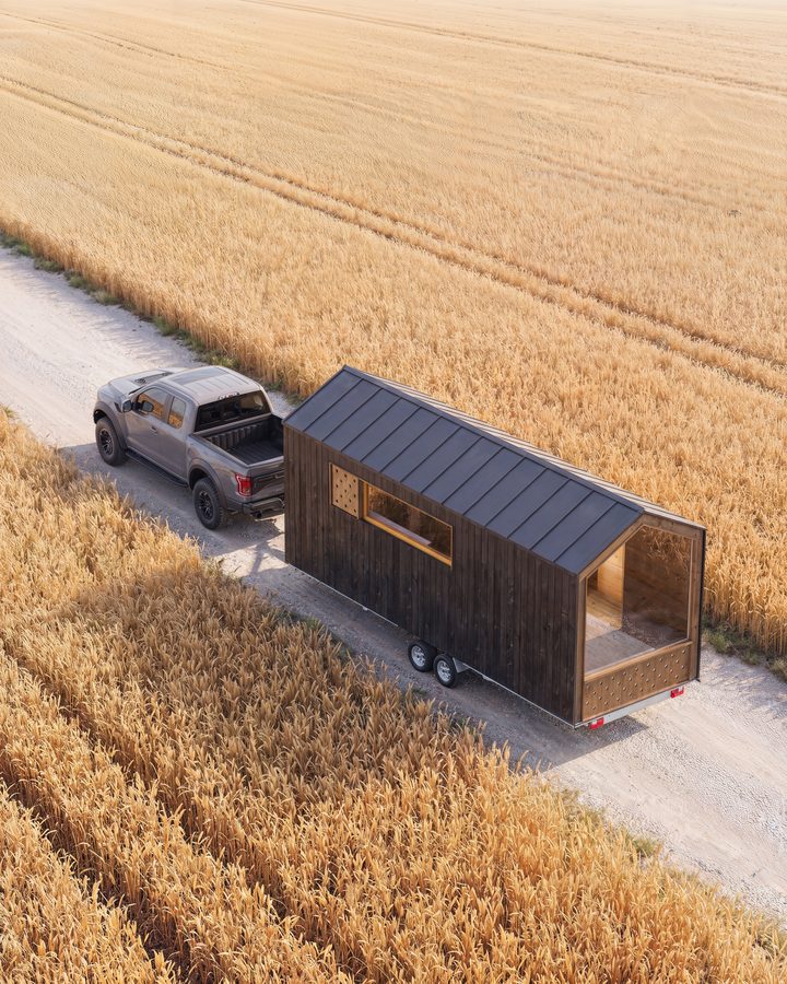 Visualisierung des THOW 2 aus der Luft: Pick-up zieht das Tiny House über einen Feldweg durch ein goldenes Weizenfeld