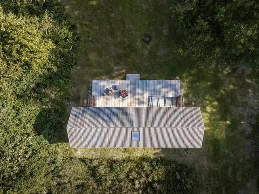 Luftaufnahme der Tinca Cabin von oben: Dach und Terrassenfläche zwischen Bäumen und Wiese