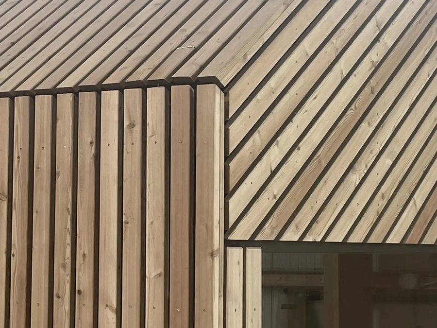 Materialdetail der Tinca Cabin: vertikale Lärchenlamellen der Thermoholzfassade am Übergang zum Fenster