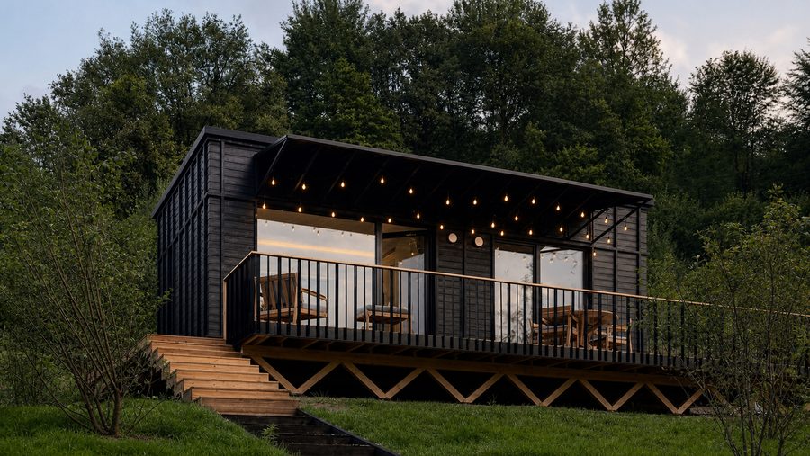 Das TR01 mit dunkler Holzfassade und umlaufender Terrasse im Grünen
