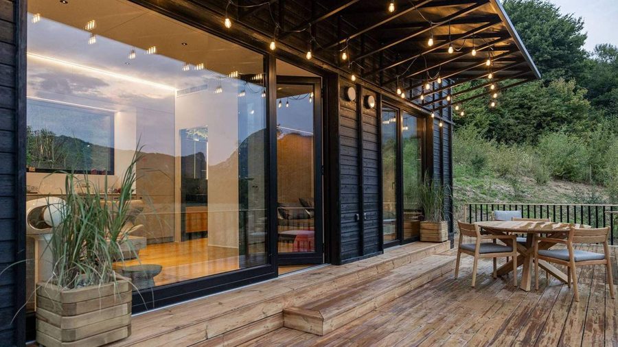 Terrasse des TR01 entlang der Verglasung: Essgruppe aus Holz, Lichterkette unter dem Vordach