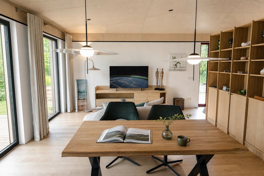Blick vom Esstisch durch den Wohnraum des TR3M-Musterhauses — Kaffee auf dem Tisch, dahinter Sofa und Gartenblick