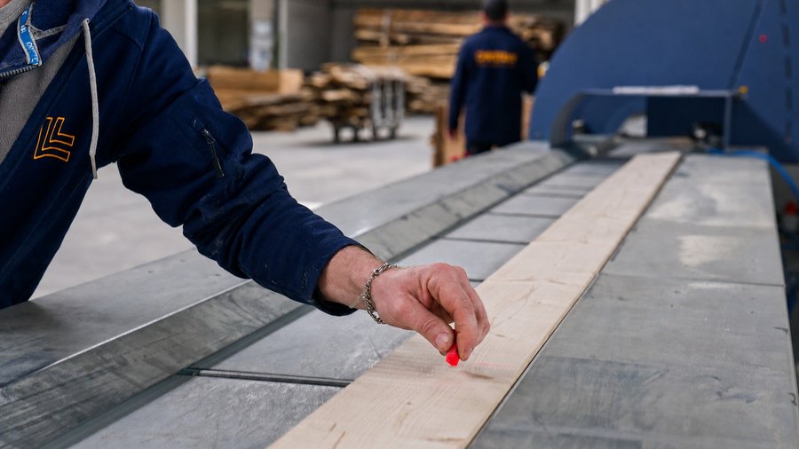 Mitarbeiter misst und markiert ein Holzbauteil in der DWELLII Fertigung