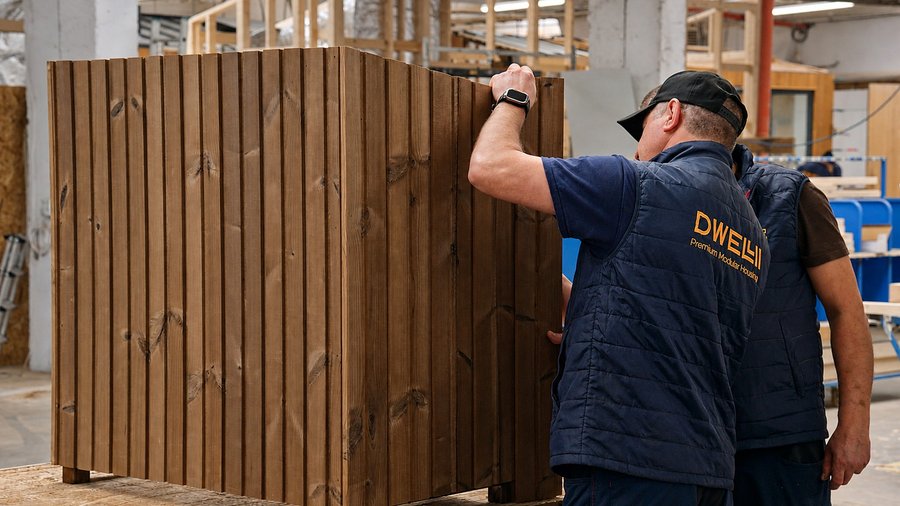 Mitarbeiter montiert eine Holzfassade an einem Hausmodul im Werk