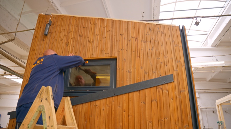 Mitarbeiter montiert präzise ein Fensterelement in die Holzfassade eines Hausmoduls