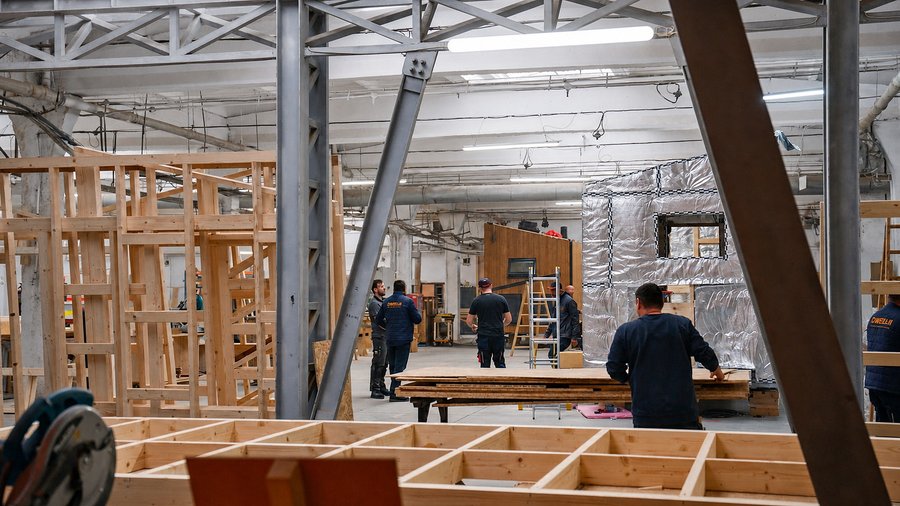 Zimmerleute arbeiten in der Werkhalle an Wandelementen, im Hintergrund ein gedämmtes Modul